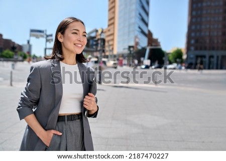 Young confident happy successful Asian business woman, professional entrepreneur, office employee wearing suit standing on city street looking in future career, thinking of success and leadership.
