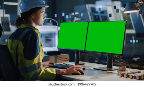 Young And Confident Industrial Female Engineer In Safety Vest And Hardhat Is Working On Computer With Green Screen Mock-up Template. Industrial Factory With High-Tech CNC Machinery