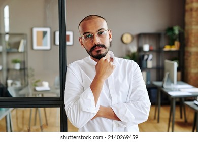 Young Confident Male Chief Executive Office Standing Against Office Interior With Several Workplaces, Shelves And Paintings On Walls