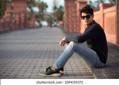 Young confident man sitting on the sidewalk of the bridge smiling, blurred view behind him in the background.