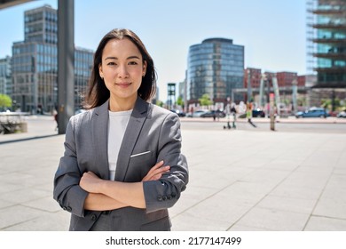 Young confident smiling Asian business woman standing on busy street, portrait. Proud successful female entrepreneur wearing suit posing with arms crossed looking at camera in big city outdoors. - Shutterstock ID 2177147499