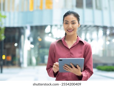 Young confident smiling asian businesswoman holding digital tablet, and standing on street at night. Beautiful Successful asian woman worker smiling and looking at camera in a city building outdoors. - Powered by Shutterstock