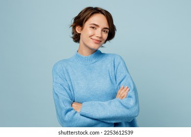 Young confident smiling happy caucasian woman wear knitted sweater look camera hold hands crossed folded isolated on plain pastel light blue cyan background studio portrait. People lifestyle concept