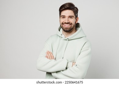 Young confident smiling happy cheerful unshaven caucasian man wear mint hoody look camera hold hands crossed folded isolated on plain solid white background studio portrait. People lifestyle concept