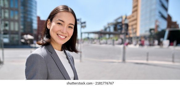 Young confident successful smiling Asian business woman entrepreneur wearing suit standing on city street advertising business trainings, corporate services, workshop, portrait. Banner with free space - Powered by Shutterstock