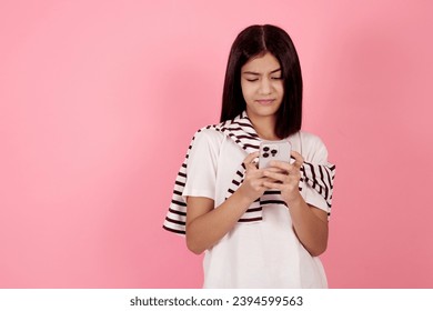 Young confident teenage girl typing on smartphone on pink background in studio. - Shutterstock ID 2394599563