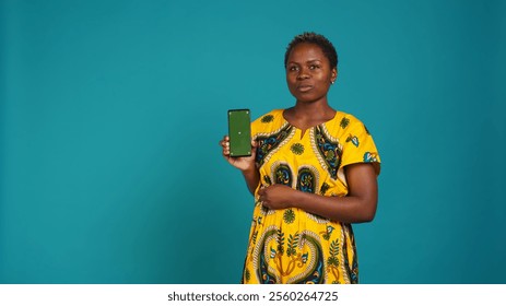 Young confident woman presenting a green screen on smartphone, working in studio on an advertisement. Smiling natural girl holds a phone with isolated chroma key display. Camera B. - Powered by Shutterstock