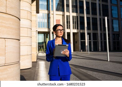 Young Confident Woman Professional Government Worker Thoughtful Looking Away While Standing With Portable Touch Pad Computer Outdoors Against Enterprise Building 