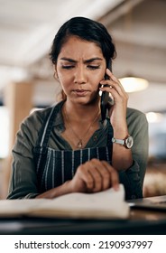 Young And Confused Business Owner On The Phone Making A Stock Order For Her Cafe, Restaurant Or Coffee Shop. A Female Employee, Manager Or Store Owner Looking At A Book Of Products Or Inventory.