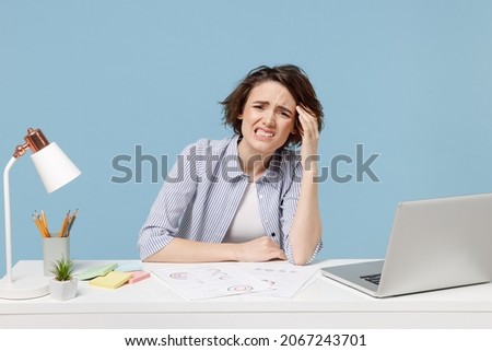 Young confused disappointed troubled secretary employee business woman in casual shirt sit work at white office desk with pc laptop prop up forehead isolated on pastel blue background studio portrait