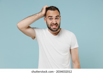 Young confused embarrassed sad puzzled man 20s wearing casual white t-shirt looking camera scratch head isolated on plain pastel light blue color background studio portrait. People lifestyle concept. - Shutterstock ID 2034032012