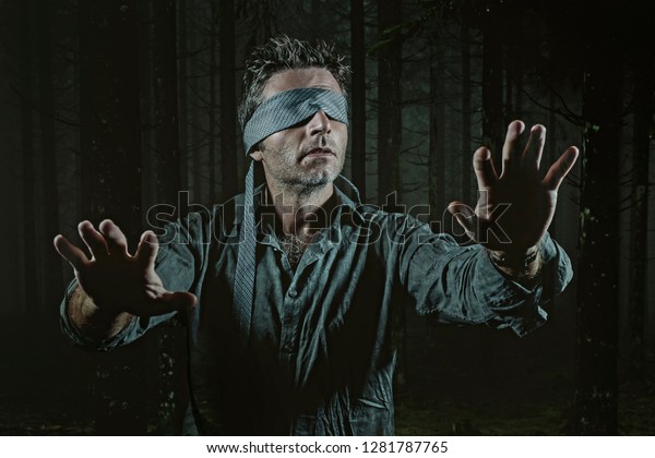 young confused and scared\
man blindfolded with necktie playing internet trend dangerous viral\
challenge with eyes blind lost in dark forest background guided by\
intuition