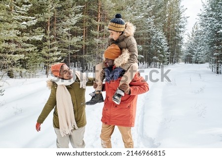 Young contemporary family of father, mother and son enjoying winter day in park while African American man carrying little boy on shoulders