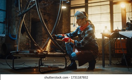 Young Contemporary Female Artist is Polishing a Metal Tube Sculpture with an Angle Grinder in a Workshop. Pretty Empowering Woman with Ear Piercing. - Powered by Shutterstock