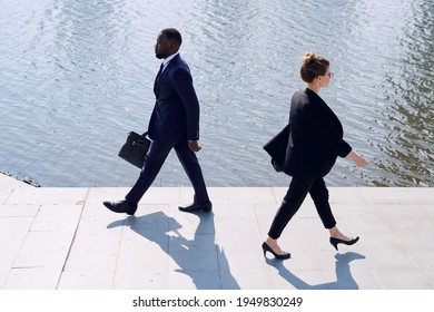 Young Contemporary Intercultural Business Professionals In Elegant Suits Moving Down Sidewalk Along Riverside While Coming Back From Work