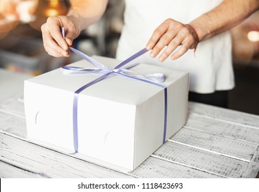 Young Cook Ties Violet Ribbon On White Cake Packaging