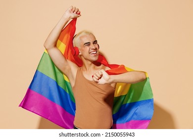 Young Cool Blond Latin Gay Man With Make Up In Beige Tank Shirt Headphones Wrapped In Rainbow Flag Listen To Music Dance Isolated On Plain Light Ocher Background Studio People Lgbt Lifestyle Concept