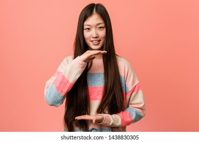 Young cool chinese woman holding something with both hands, product presentation.
