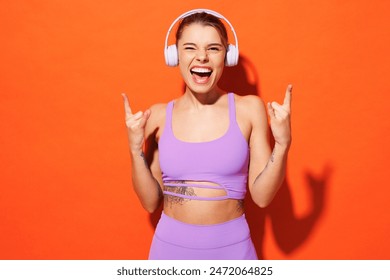 Young cool fun fitness trainer instructor sporty woman sportsman wear purple top clothes in home gym listen to music in headphones isolated on plain orange background. Workout sport fit abs concept - Powered by Shutterstock