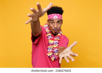 Young Cool Fun Man 20s He Wear Pink T-shirt Hawaiian Lei Bandana Near Hotel Pool Stretching Hands To Camera Isolated On Plain Yellow Background Studio Portrait. Summer Vacation Sea Rest Vibe Concept