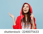 Young cool happy woman of African American ethnicity 20s wear red raincoat hood spead hand catch rain drops isolated on plain pastel light blue cyan color background. Wet fall weather season concept