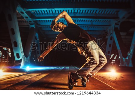 Young cool man break dancer on urban bridge with cool and warm lights background. Tattoo on body.
