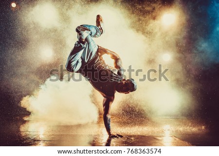Young cool man break dancing in club with lights, smoke and water. Tattoo on body.