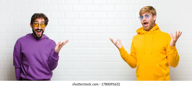 young cool men feeling happy  excited  surprised shocked  smiling   astonished at something unbelievable against white tiles wall