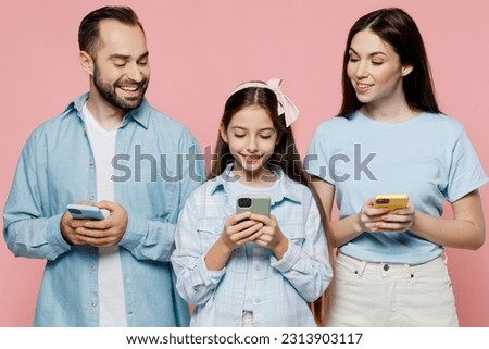Young cool parents mom dad with child kid daughter teen girl in blue clothes hold in hand use mobile cell phone peeps isolated on plain pastel pink background. Family day parenthood childhood concept