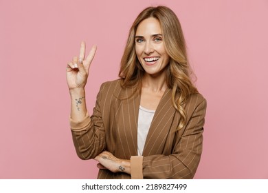 Young cool smiling happy fun friendly cheerful successful employee business woman 30s she wearing casual brown classic jacket showing victory sign isolated on plain pastel light pink background studio