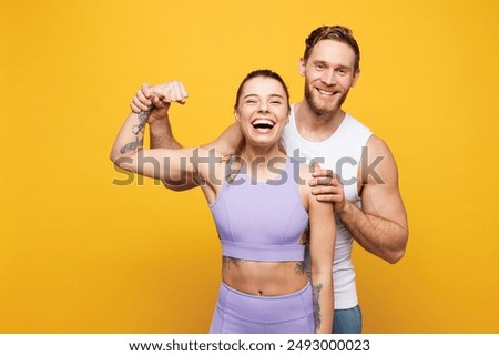 Young cool strong fitness trainer instructor sporty two man woman wear blue clothes spend time in home gym showing biceps muscles on hand isolated on plain yellow background. Workout sport fit concept