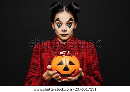 Young cool woman with Halloween makeup face art mask wears clown costume red dress hold Jack-o-Lantern carved pumpkin isolated on plain black background studio portrait. Scary holiday party concept