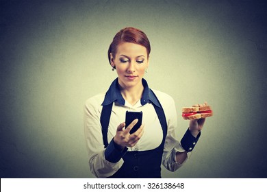 young corporate business woman reading news message on smart phone holding eating sandwich isolated on gray wall background. Human face expression. Social media app