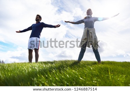 Young couple in activewear standing on green field with their arms outstretched