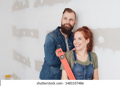 Young couple admiring their DIY renovation work on their home standing holding a spirit level and smiling happily in satisfaction