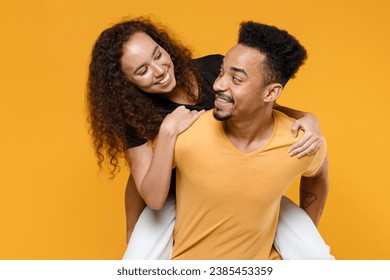 Young couple of African American ethnicity two friends family man woman wear black t-shirt giving piggyback ride to joyful sit on back look to each other isolated on yellow background studio portrait - Powered by Shutterstock