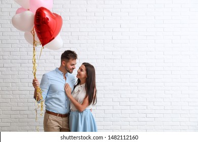Young couple with air balloons near white brick wall. Celebration of Saint Valentine's Day