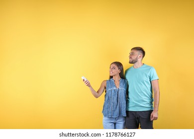 Young couple with air conditioner remote on color background, copy space text