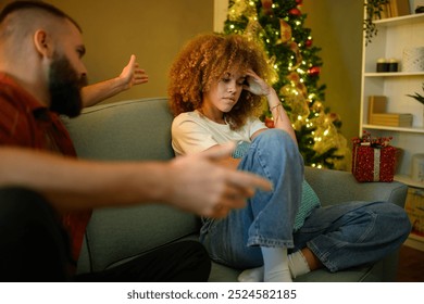 Young couple argues on the sofa amid christmas decorations, showing tension and communication issues during the festive season - Powered by Shutterstock