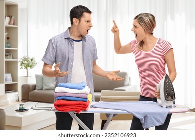 Young couple arguing behind an ironing board at home in a living room - Shutterstock ID 2352106923