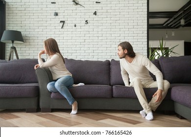 Young couple arguing sitting on sofa, man shouting at woman on couch in living room, offended wife not talking to husband, dissatisfied boyfriend blaming girlfriend, family problems, marital conflict