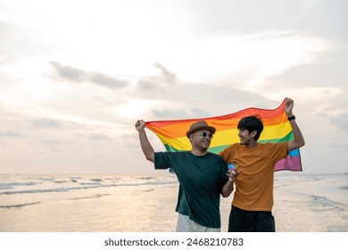 Young couple asian gay with pride movement LGBT holding rainbow flag raise up for freedom. Demonstrate rights LGBTQ celebration pride Month Gay Pride Symbol. Walking on the sand sea beach with sunset - Powered by Shutterstock