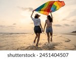 Young couple asian lesbian with pride movement LGBT holding rainbow flag for freedom. Demonstrate rights LGBTQ celebration pride Month lesbian Pride Symbol. Walking on the sand sea beach with sunset