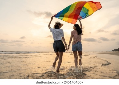 Young couple asian lesbian with pride movement LGBT holding rainbow flag for freedom. Demonstrate rights LGBTQ celebration pride Month lesbian Pride Symbol. Walking on the sand sea beach with sunset - Powered by Shutterstock