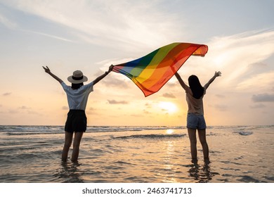Young couple asian lesbian with pride movement LGBT holding rainbow flag for freedom. Demonstrate rights LGBTQ celebration pride Month lesbian Pride Symbol. Walking on the sand sea beach with sunset - Powered by Shutterstock
