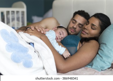 Young couple asleep in bed with their baby son sleeping on his mothers chest.