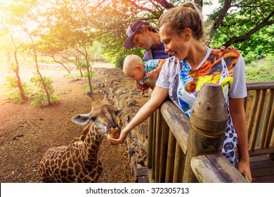 young couple with a baby feeding a giraffe at the zoo on a jungle background. The child laughs. Mauritius Casela Safari Park - Shutterstock ID 372305713