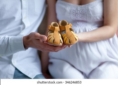 The young couple with baby shoes sitting on sofa at home