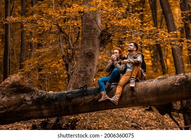 Young couple with backpack sitting on collapsed trunk resting and drinking tea after hiking in forest. - Powered by Shutterstock