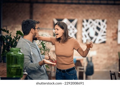 Young couple in a bar having an argument. Woman mad at man and holding his mouth shut.  - Powered by Shutterstock